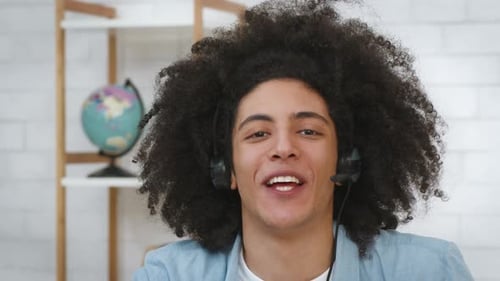 College Student Guy Wearing Headset Waving Hello To Camera Indoors