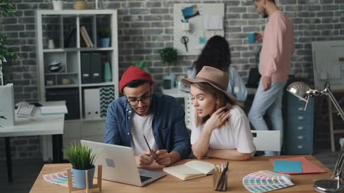 Man and Woman Working Together Looking at Laptop Screen Sitting in Office