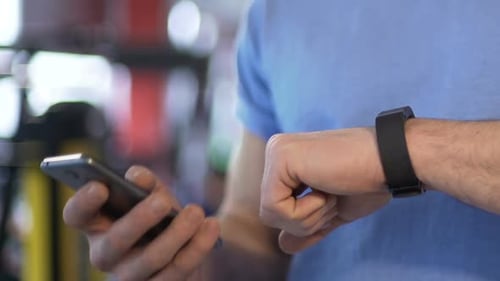 Guy synchronizing mobile phone with smart watch in gym before training session