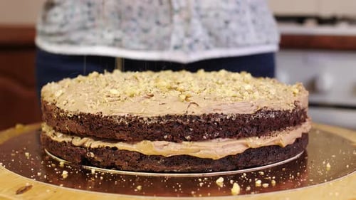 Chocolate Cake Being Drizzled with Crushed Nuts