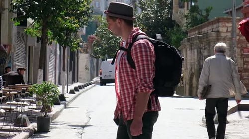 Young Man Tourist with Hat and Backpack Walking in a Touristic City Looking to Streets