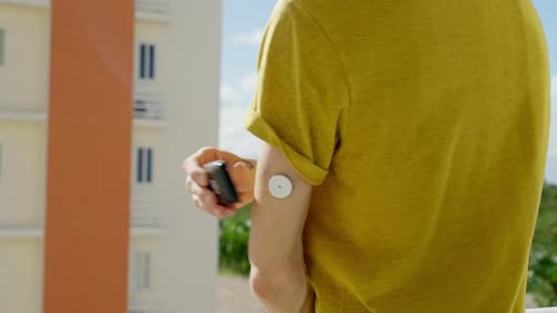Male Checking His Blood Glucose Levels On Left Arm With Freestyle Libre 2 Sensor On Hotel Balcony