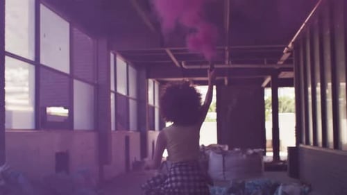 Mixed race woman holding purple flare running through an empty building