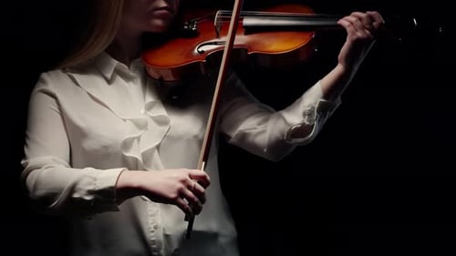 Woman Musician in a Blouse Removes Violin From the Shoulder and Lowers Bow Standing in a Dark Studio