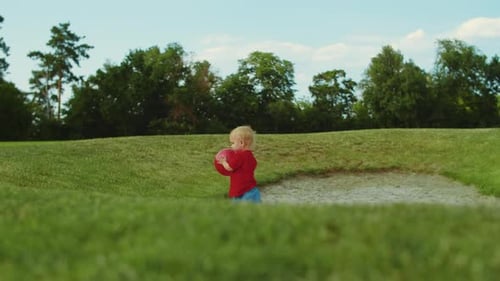 Boy Walking in Green Field. Cheerful Child Holding Ball in Hands Outdoors