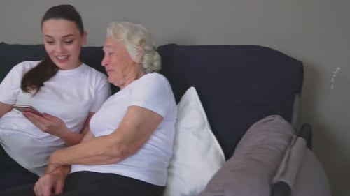 Smiling Grandmother and Granddaughter Using Smartphone on Couch