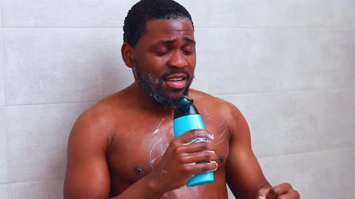 Attractive Young Cheerful Man Singing While Washing in the Shower Holding Shampoo Bottle