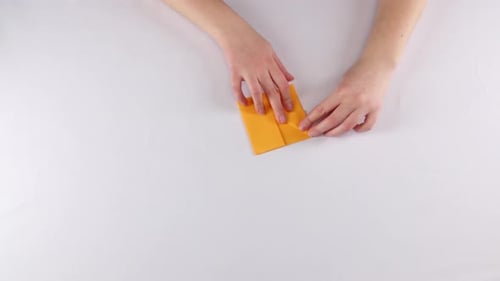 Hands Folding Orange Paper to Create Geometric Form