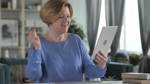 Mature Woman Celebrates Success Using Tablet at Home