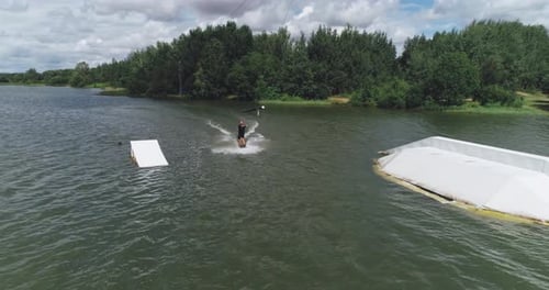 Wakeboarden in einem See in Waldnähe, Sportler surft auf dem Wasser, Fahrt auf einem Wakeboardboard