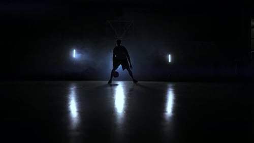 Ein Mann mit einem Basketball auf einem dunklen Basketballplatz vor dem Hintergrund eines Basketballrings in der