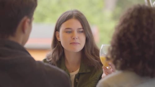 Company of Three Friends Enjoying Juice Sitting Together in the Cafe Outdoors