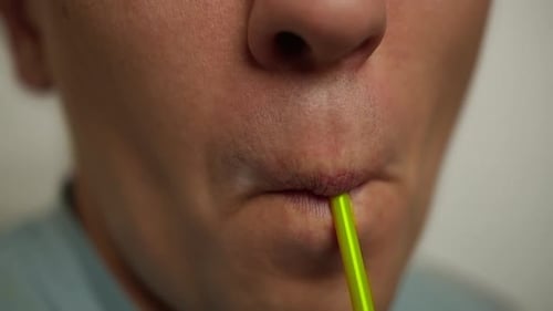 Young man drinking a drink from a plastic cocktail tube, close-up