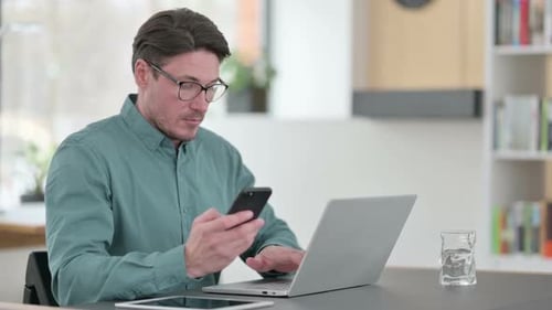Focused Man Using Laptop and Smartphone at Desk
