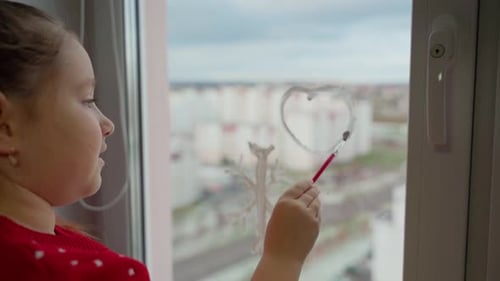 Child draw heart on window with white paints close-up. Caucasian female person decorate living room