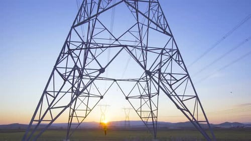 Power Line Tower on Grassy Field at Sunset