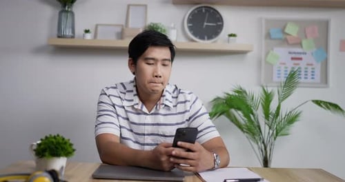 Asian man holding smartphone texting message in home office