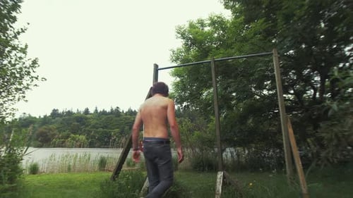 Un jeune homme aux seins nus en forme entre dans le cadre et saute pour tirer vers le haut de la barre de gym à la maison