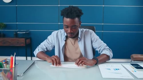 Junger Afroamerikaner startet Papierflugzeug, das im Büro am Tisch sitzt