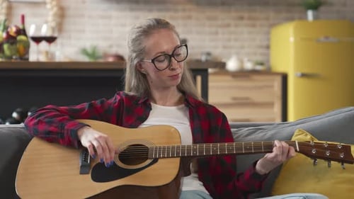 Woman Playing Acoustic Guitar on Couch Indoors