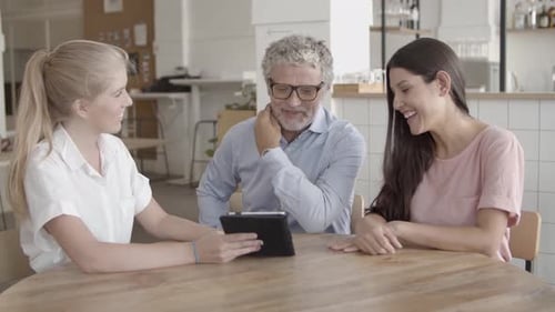 Three People Talking and Using Tablet at Table