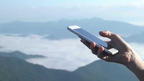 Hand Holding Phone Above Mountain Landscape