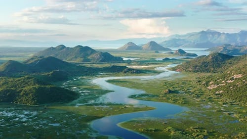 Bends and curves of blue river flowing through green valley toward distant mountains.