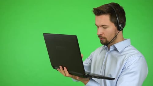 A Young Call Center Agent Works on a Notebook and Talks To a Caller, Then Smiles - Green Screen