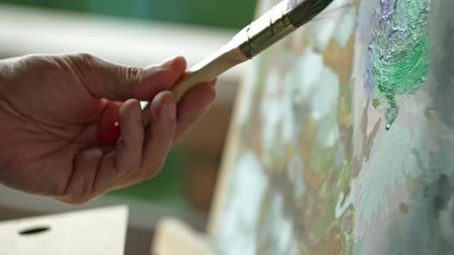 Closeup of a Brush Dipping Into Paint and a Man's Hand Painting a Picture