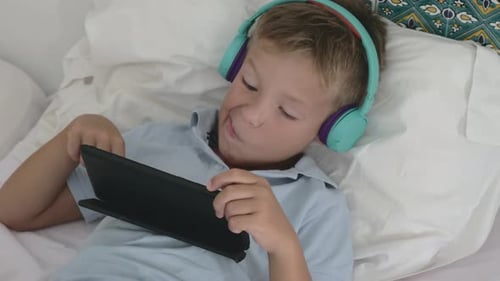 Boy Playing Tablet, Wearing Headphones in Bed