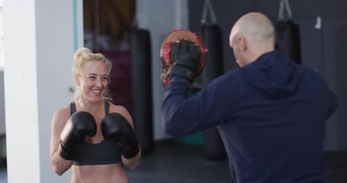 Caucasian female boxer wearing boxing gloves training her punches with male trainer at the gym