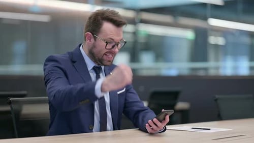 Middle Aged Businessman Celebrating Success on Smartphone