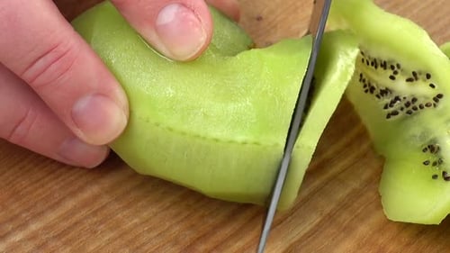 Hands Slice a Fresh Green Kiwi on Board