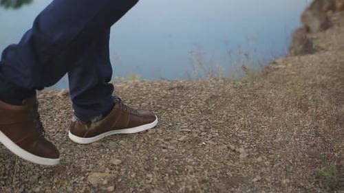 Nahaufnahme der Beine eines Mannes, der am Ufer eines Teiches entlang geht