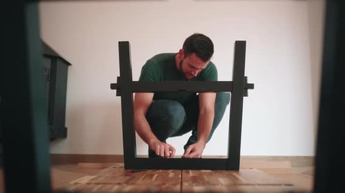 Front View Of A Man Screwing Metal Legs Onto Table Top. Assembling DIY Table In The House. static