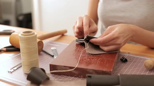 Person Sewing Leather at Wooden Workbench