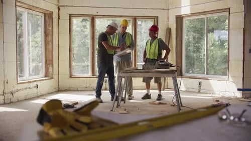 Drei Bauarbeiter schauen sich Baupläne auf einer kommerziell Baustelle an