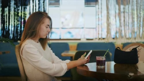 Joyful Girl Drinking Tea in a Cafe and Talking on the Phone or Video Call