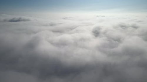 Aerial shot of flying over a layer of soft clouds at dawn