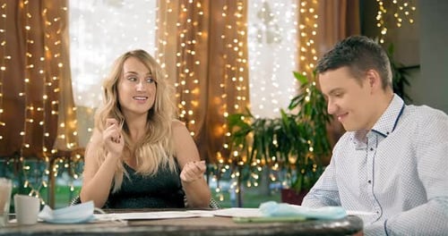 Blonde Woman Dances at Table and Guy Reads Menu in Cafe