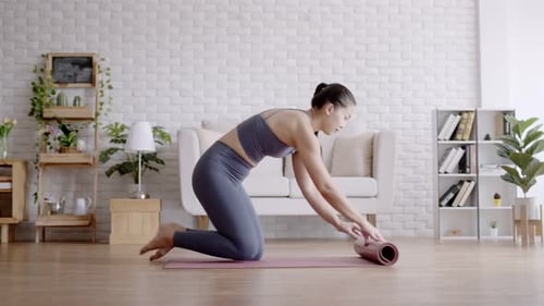 Asian woman preparing for sports training and unrolling her exercise mat on the floor.