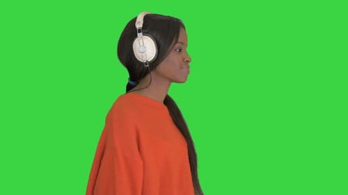 Smiling African American Woman with Headphones Walking Listening To the Music on a Green Screen