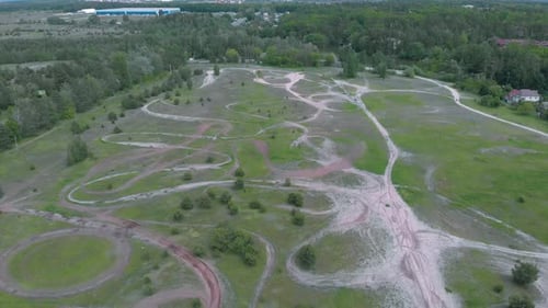 Motocross motorcycle track with enclosed dirt circuits with steep obstacles surrounded by forest.