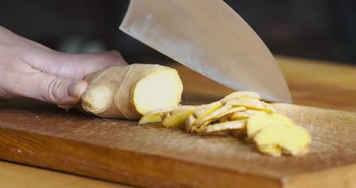 Femme coupant la racine de gingembre fraîche sur la table de cuisine en gros plan