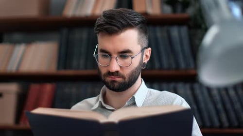 Selbstbewusster bärtiger Hipster-Mann liest Vintage-Papierbuch in der öffentlichen Bibliothek