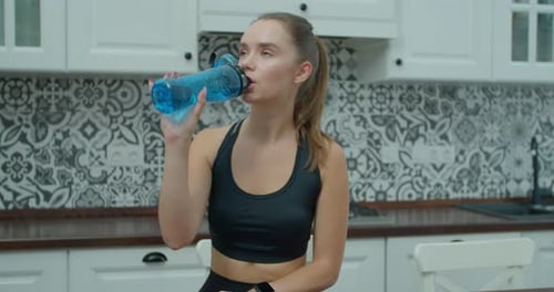 Woman Drinks Water in Kitchen After Workout