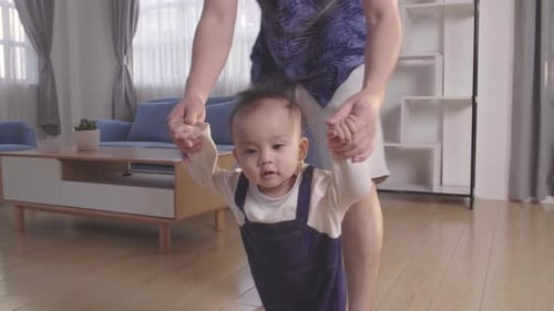 Baby Boy Learning To Walk And Make His First Steps. Father Is Holding His Hand