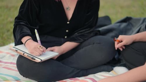 Close Up on Girl Hand Writing on a Notepad While Sit on Ground