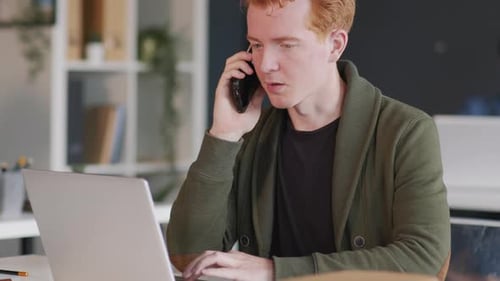 Young Adult Talking on Phone While Working on Laptop