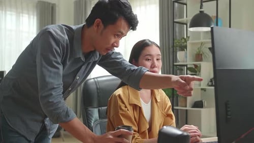 Asiatische Frau diskutiert mit Mann, während sie im Büro am Computer arbeitet